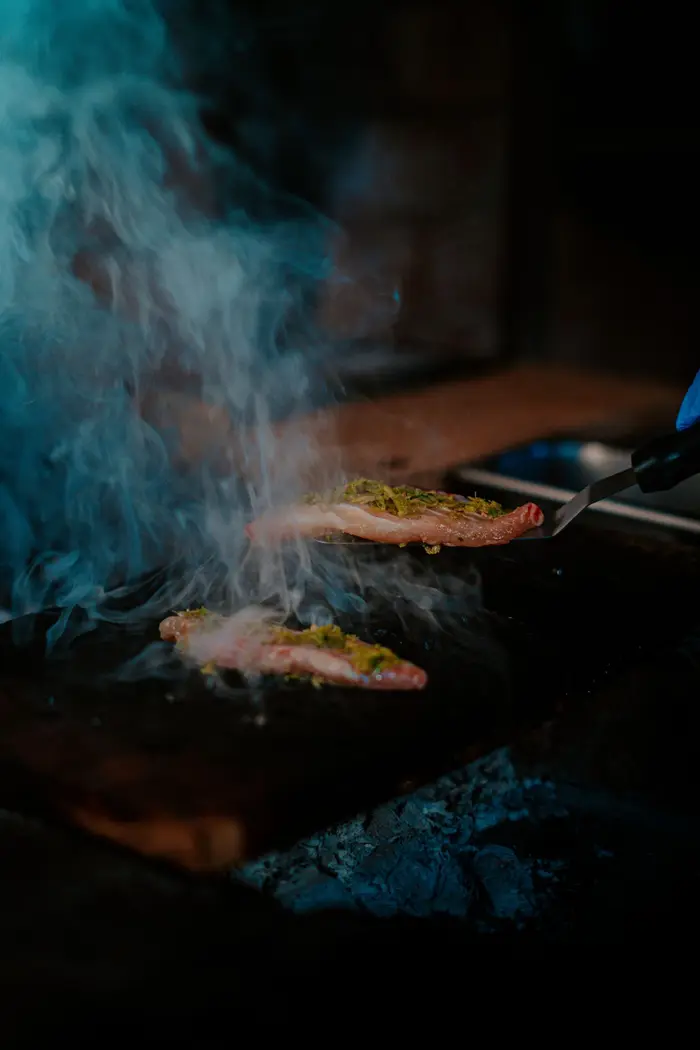 Fish cooking over smoke on a neem plank