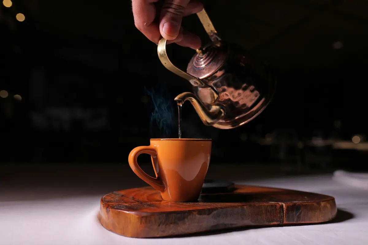 Mint tea poured from a copper kettle into a clay cup